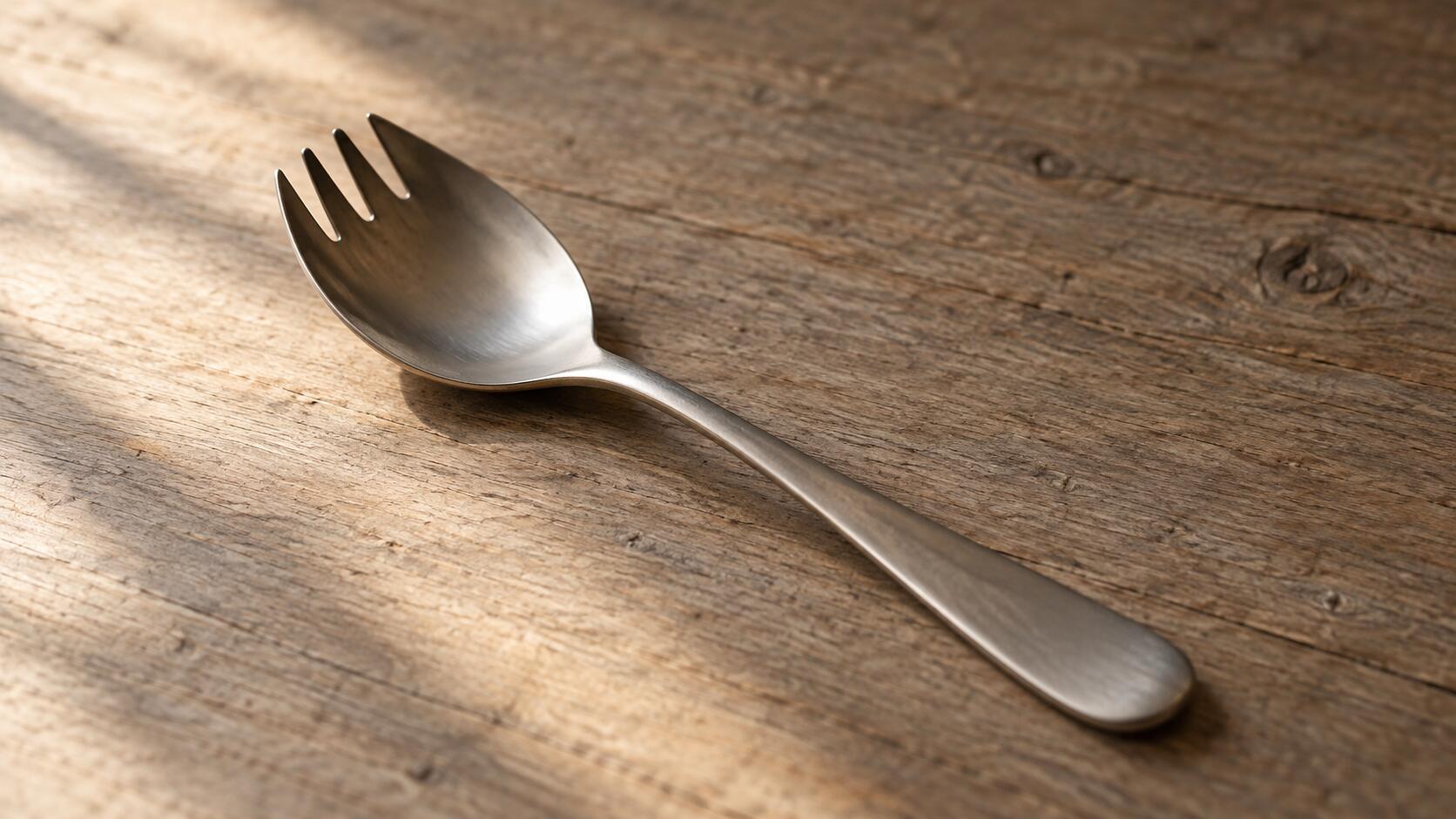 A single spork resting on a wooden table in warm light.